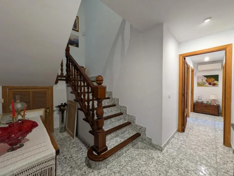 Un pasillo embaldosado con una escalera y una puerta abierta a una habitación contigua.