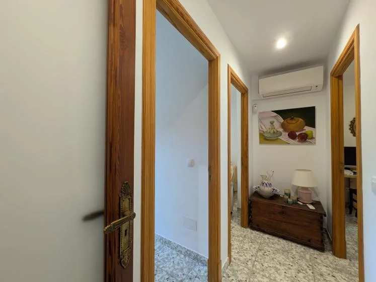 Un pasillo con puertas de madera, suelo de baldosas estampadas y una cómoda pequeña.