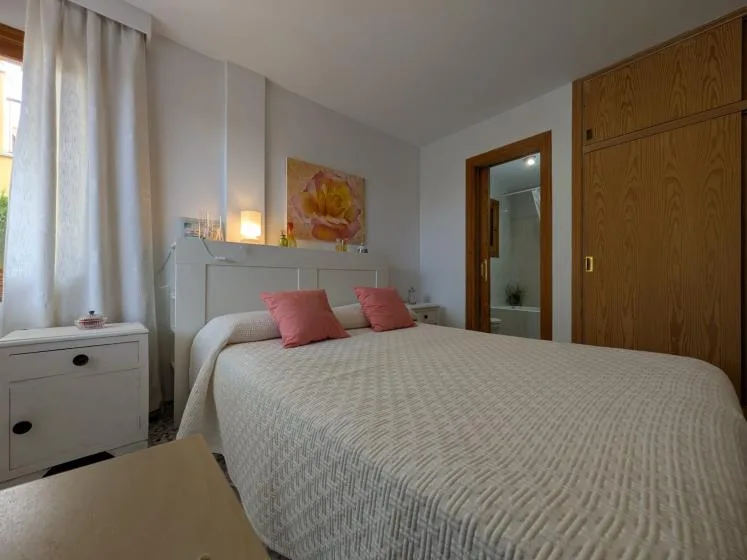 Un dormitorio con una cama bien tendida y cojines rosas junto a un armario de madera.