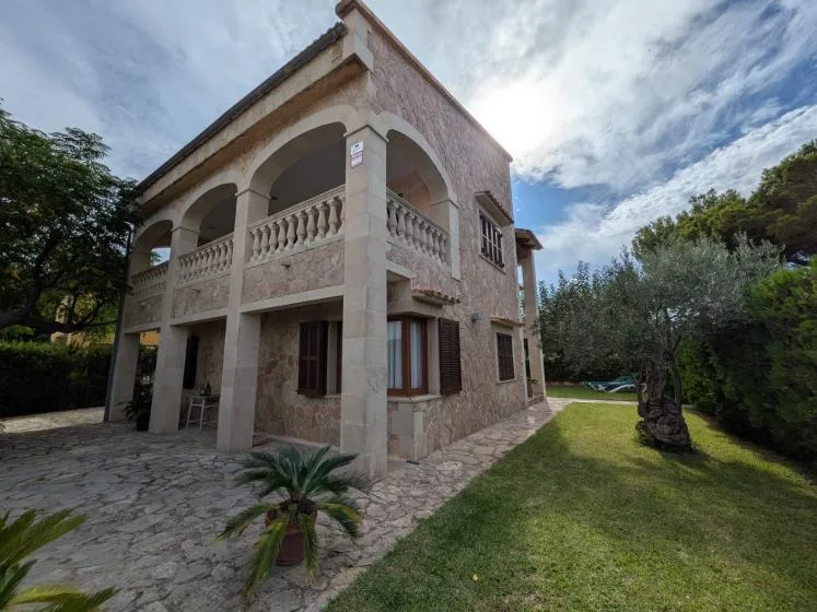 A stone house with arched balconies stands beside a grassy yard.