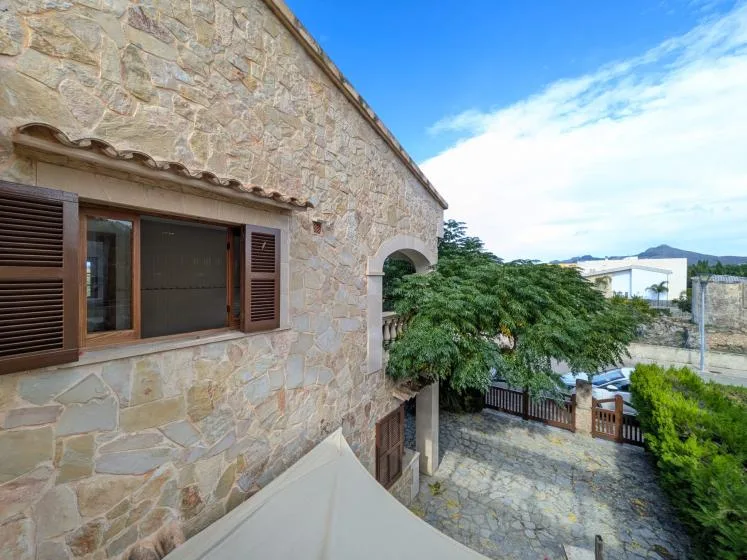 El exterior de una casa de piedra da a un patio pavimentado con árboles y una puerta.