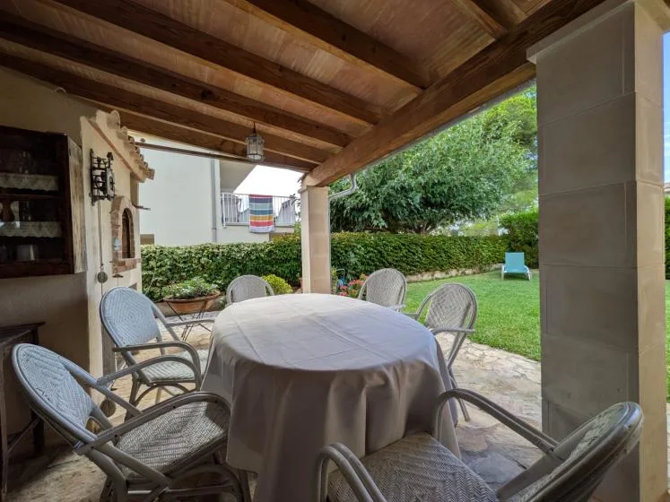 A covered patio dining area with a round table and chairs beside a green lawn.