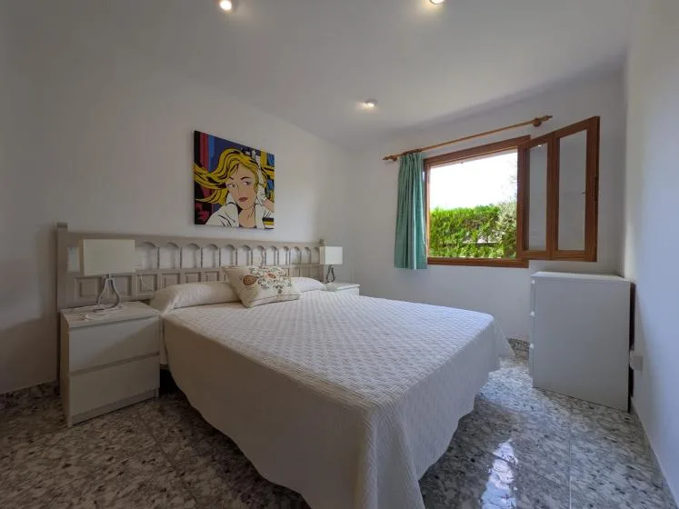 Un dormitorio luminoso con una cama grande, arte colorido en la pared y una ventana abierta.