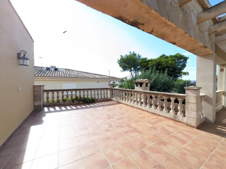 Una amplia terraza de baldosas con una balaustrada de piedra y árboles al fondo.