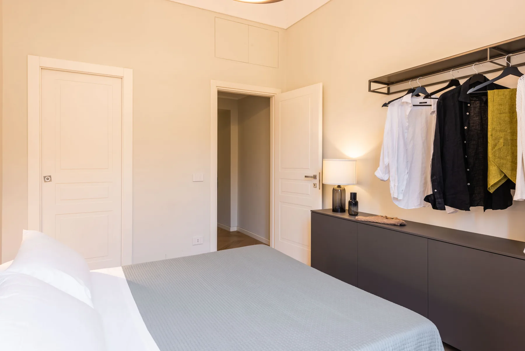 Un dormitorio con una cama, una puerta abierta y ropa colgada sobre un armario.