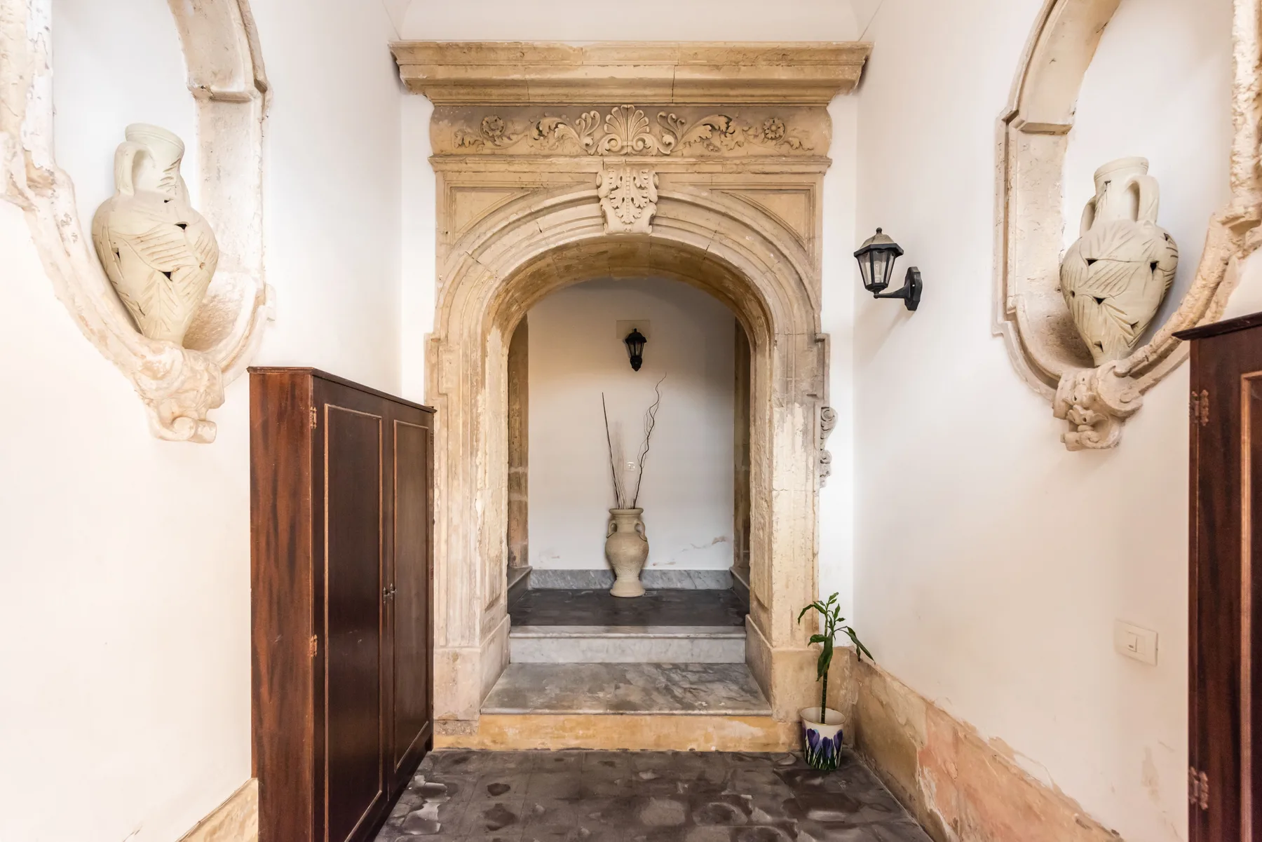 Un pasillo con un arco ornamentado, una puerta de piedra decorativa y una planta en maceta.