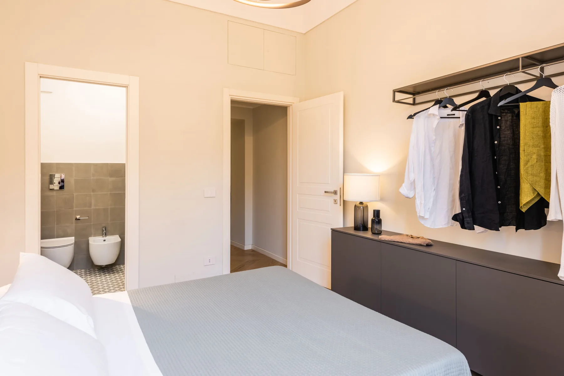 Un dormitorio con una cama, una puerta abierta y ropa colgada en un perchero.