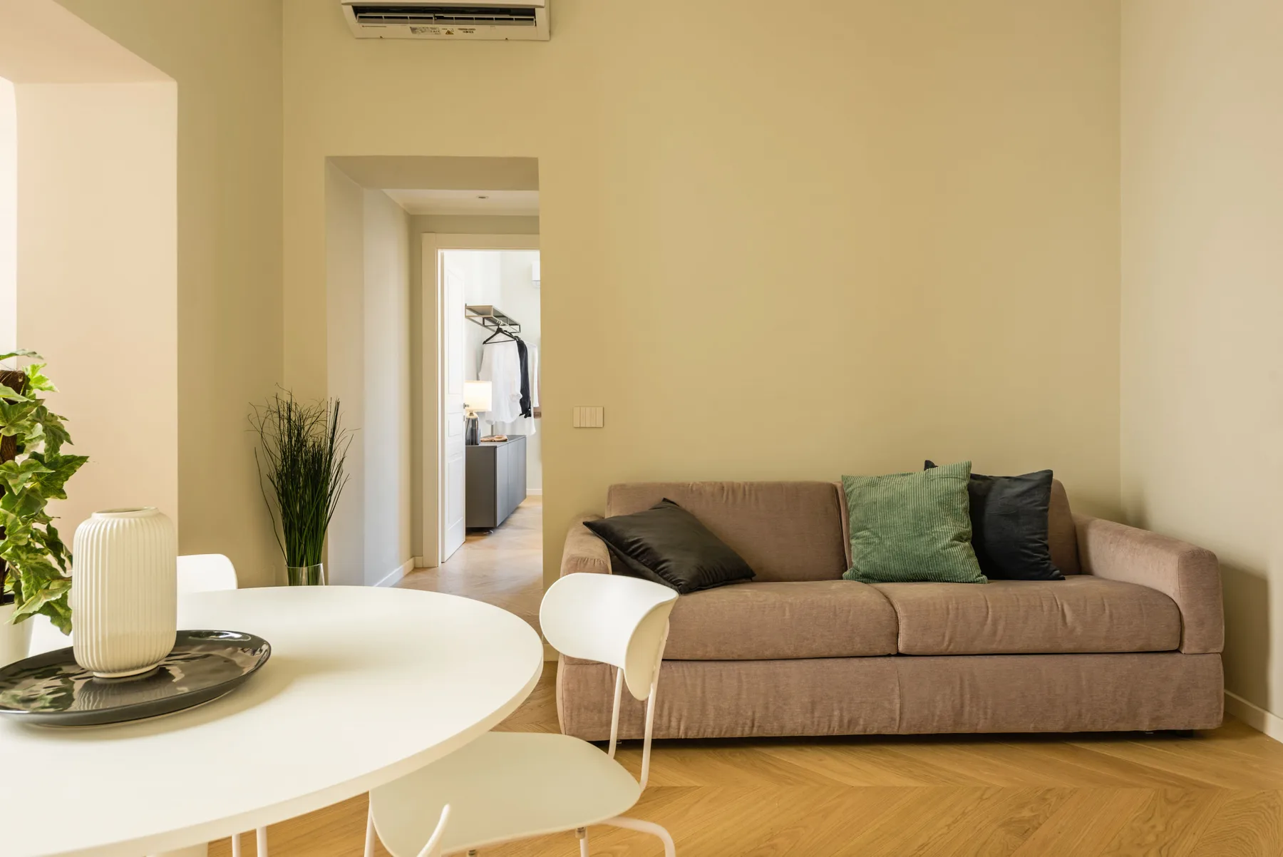 Una sala de estar con un sofá, una mesa redonda y una puerta hacia otra habitación.