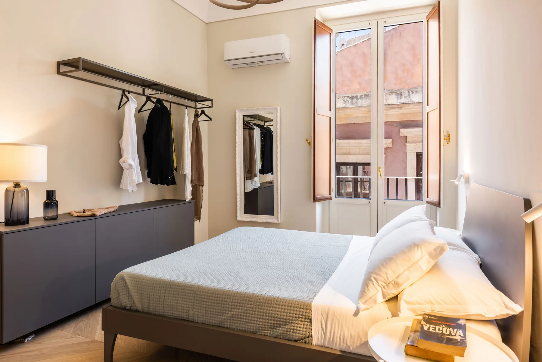 Un dormitorio con una cama, un perchero de pared y ventanas altas.