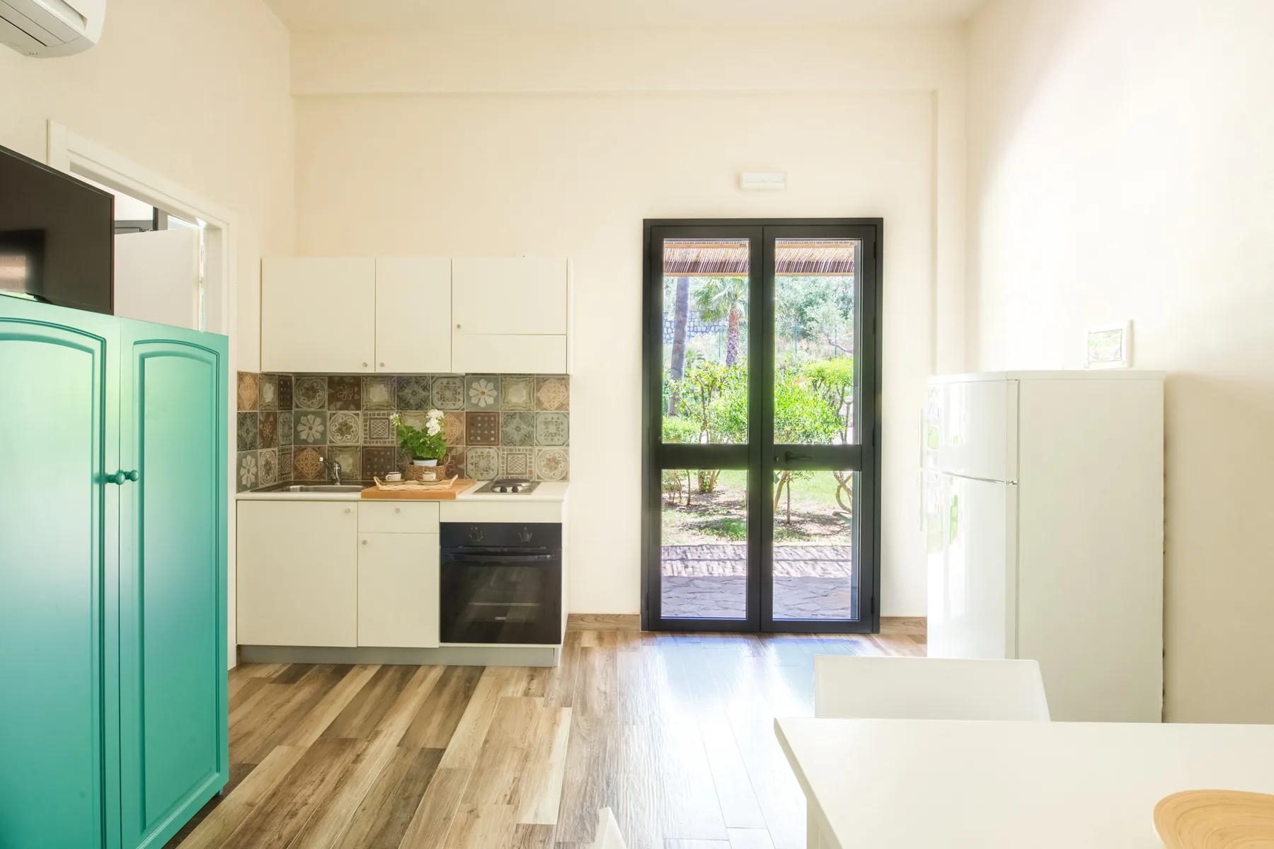A bright kitchen with white cabinetry, a tiled backsplash, and glass doors opening to greenery.