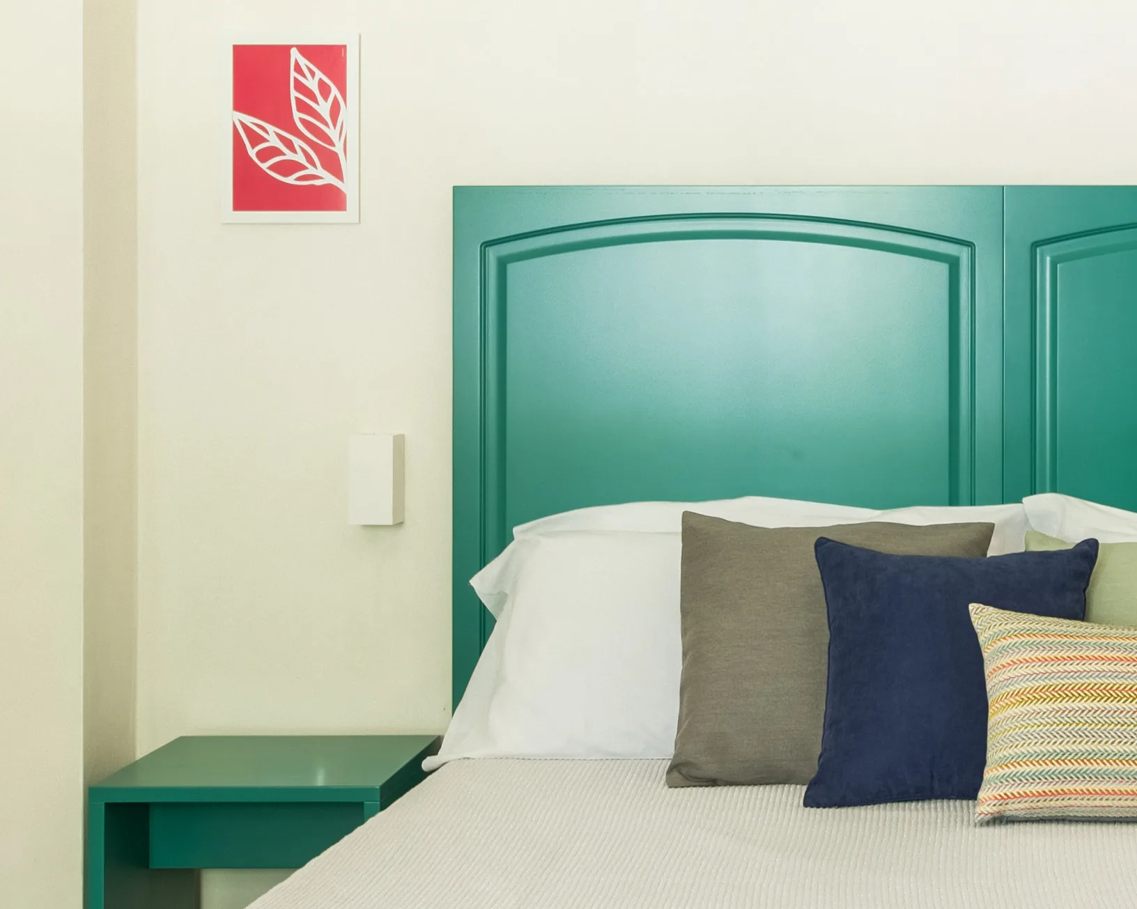 A bedroom with a bed, colorful pillows, and a teal headboard.
