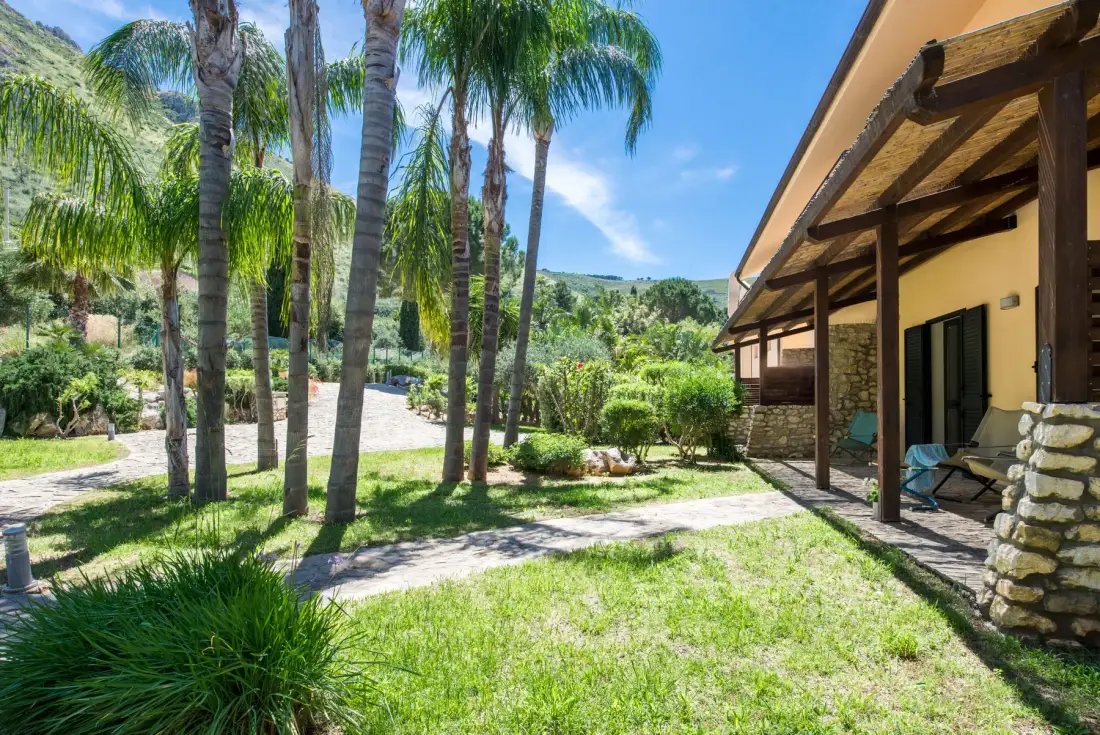 A sunny outdoor patio beside a building, surrounded by palm trees and green landscaping.