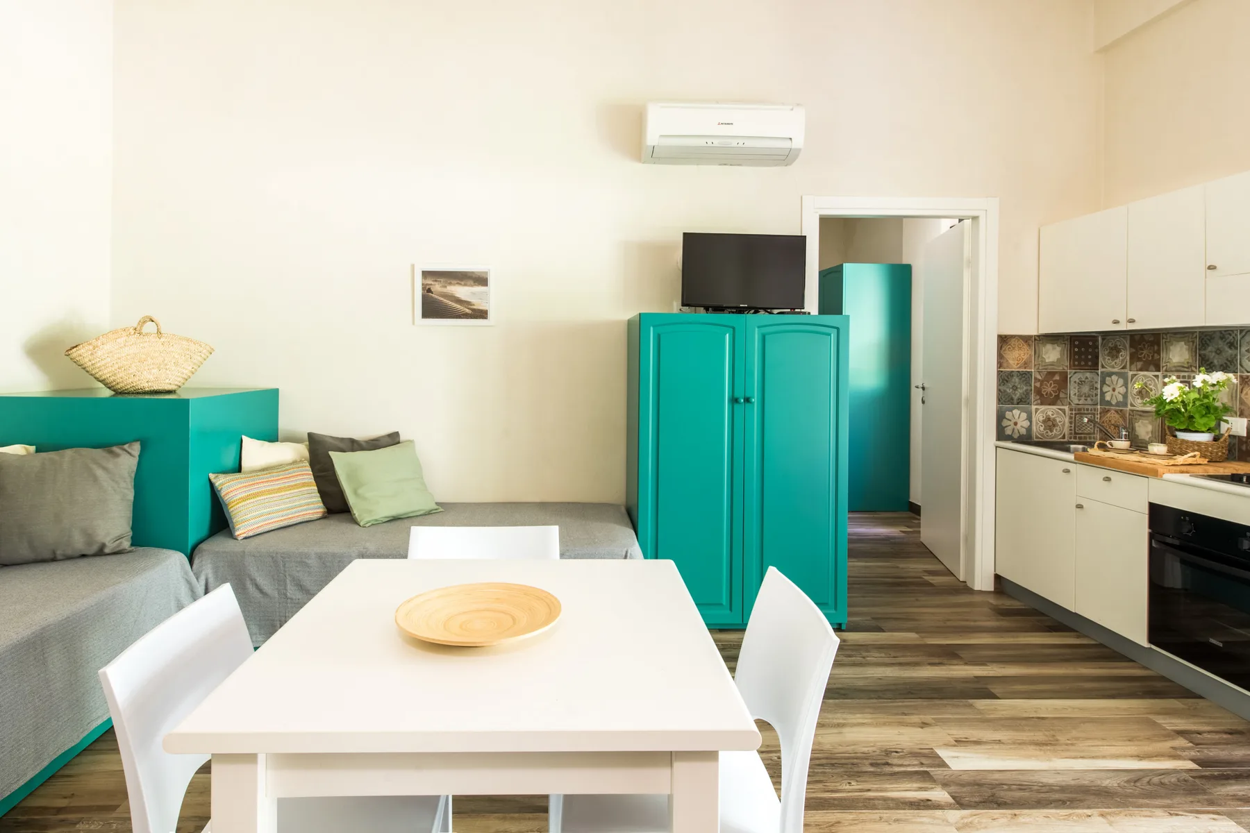 A dining area with white table and chairs beside teal cabinets and gray seating.