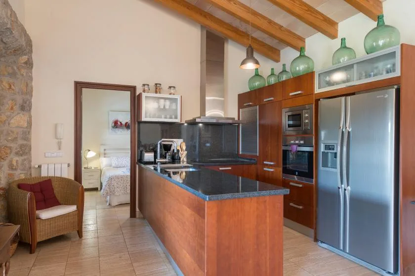 A kitchen with a wood-fronted island, stainless steel refrigerator, and exposed ceiling beams.
