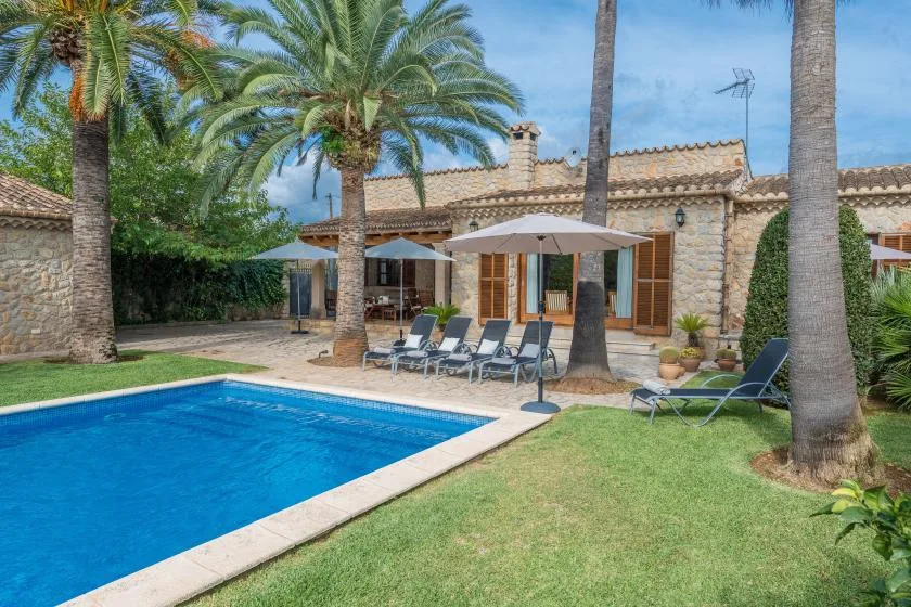 A swimming pool and lawn sit in front of a stone house with palm trees.