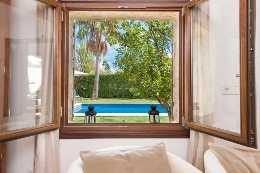 A bedroom window overlooks a swimming pool and leafy garden.
