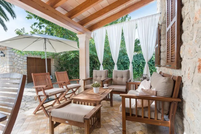 A covered outdoor seating area with wooden furniture and white curtains.