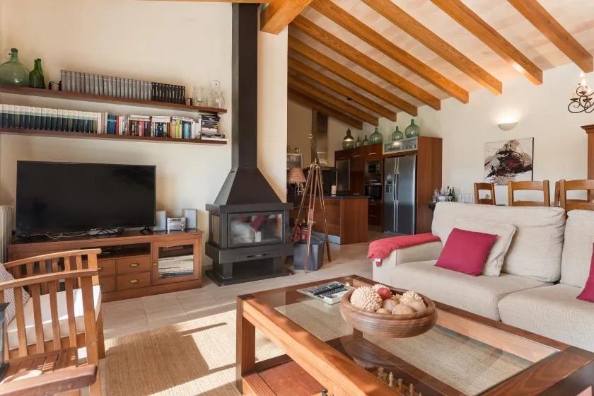 A living room with seating, a television, and a wood-burning stove beneath exposed beams.
