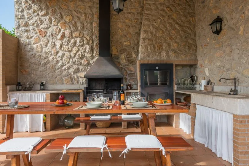 An outdoor dining area with a long table and a stone cooking hearth.