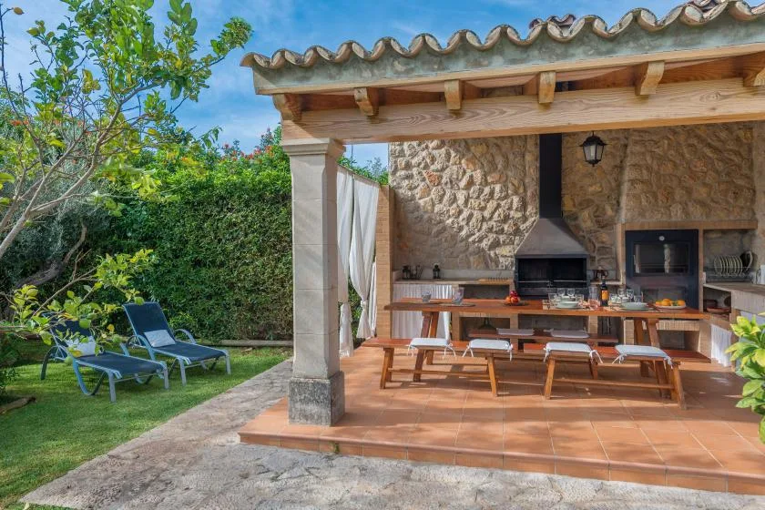 A covered outdoor dining area with a long table and built-in barbecue.
