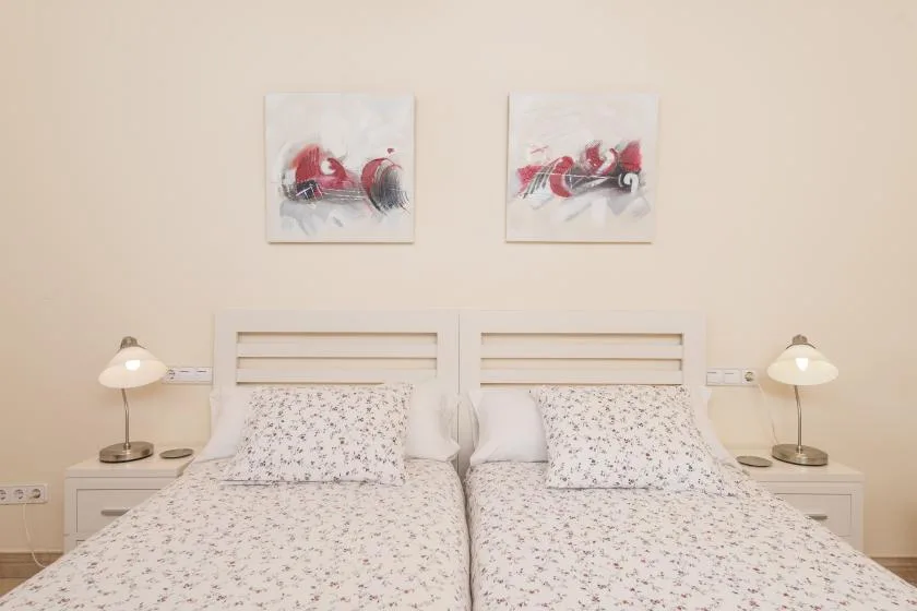 A bright bedroom with two beds, matching bedside lamps, and abstract artwork.