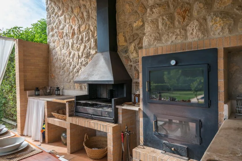 An outdoor cooking area with a stone wall, built-in grill, and wood-fired oven.