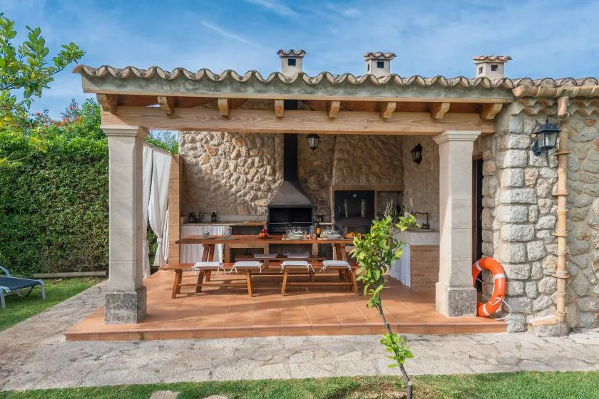 A covered outdoor dining area with a long wooden table and built-in grill.