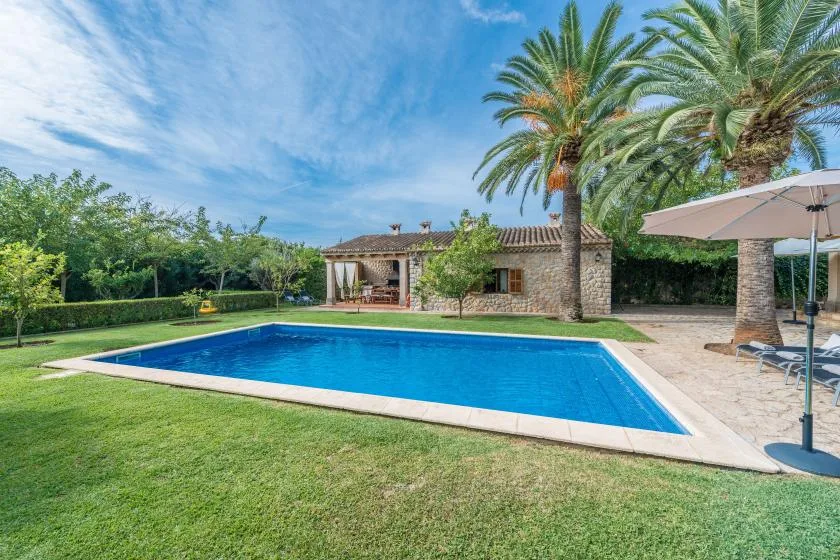 An outdoor swimming pool sits beside a lawn and a low stone building.