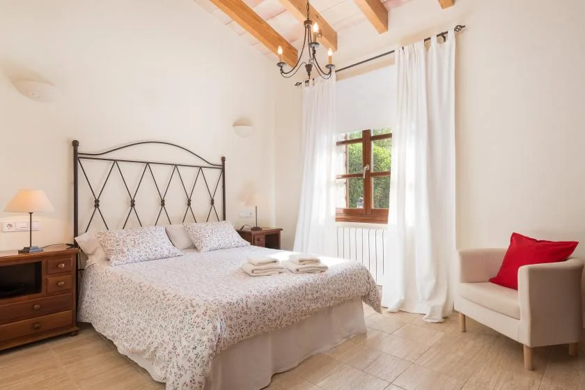 A bright bedroom with a double bed, bedside tables, and a window with curtains.