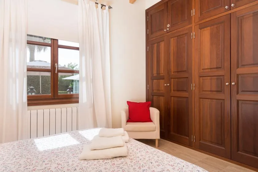 A bedroom with a bed, a window, and built-in wooden wardrobes.