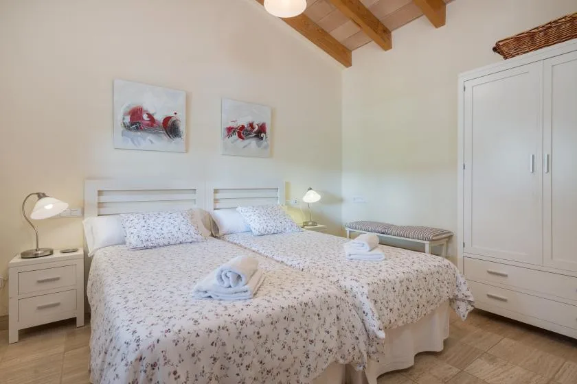 A bright bedroom with two beds, bedside tables, and a white wardrobe.
