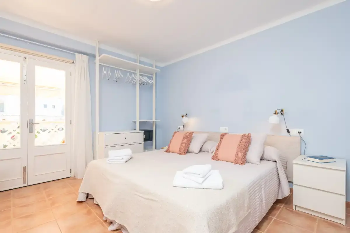 Un dormitorio luminoso con una cama bien hecha y un armario abierto.