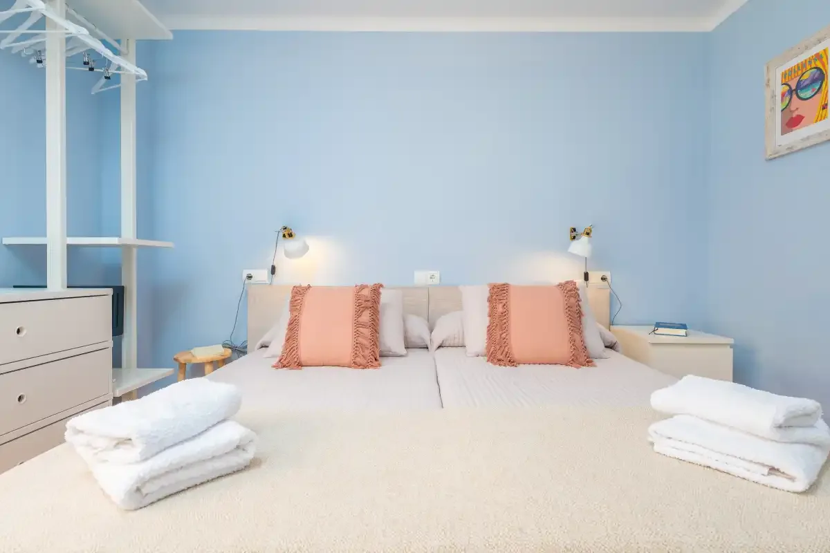 Dormitorio con una cama, paredes azul claro y toallas dobladas.