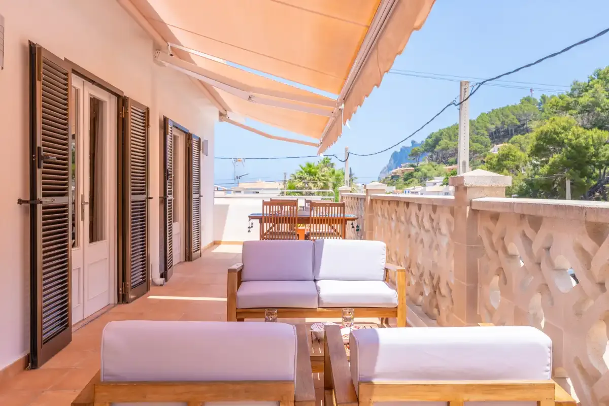 Una terraza cubierta tiene asientos al aire libre y una balaustrada de piedra con vistas a la vegetación.