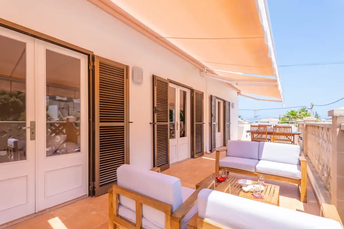 Una terraza soleada con asientos acolchados y un toldo naranja.