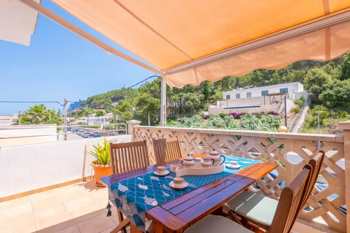 Una terraza comedor a la sombra ofrece vistas de casas en la ladera y vegetación.