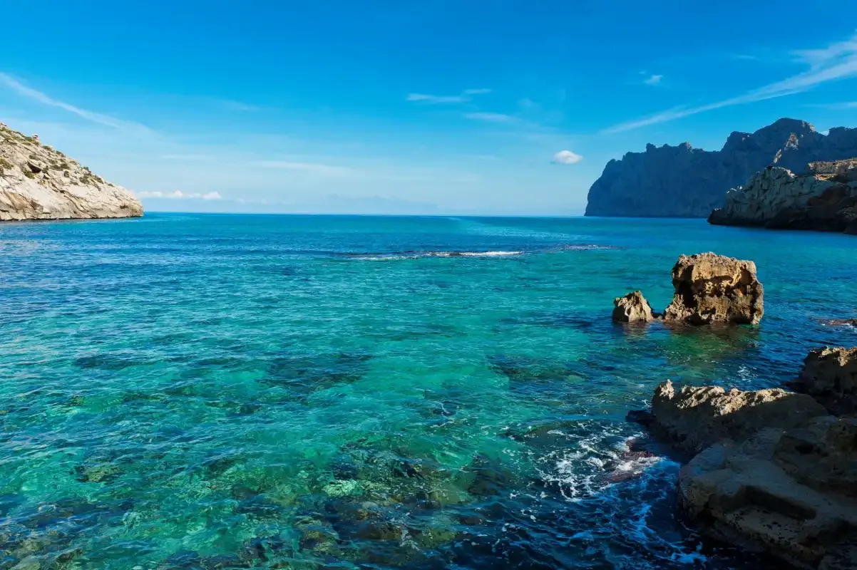 El mar azul y transparente se extiende entre acantilados rocosos bajo un cielo despejado.