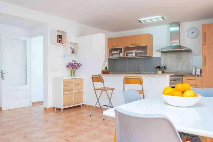 Una cocina luminosa con zona de comedor, mesa blanca y armarios de madera.