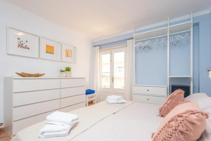Un dormitorio con una cama, una cómoda blanca y un perchero abierto.