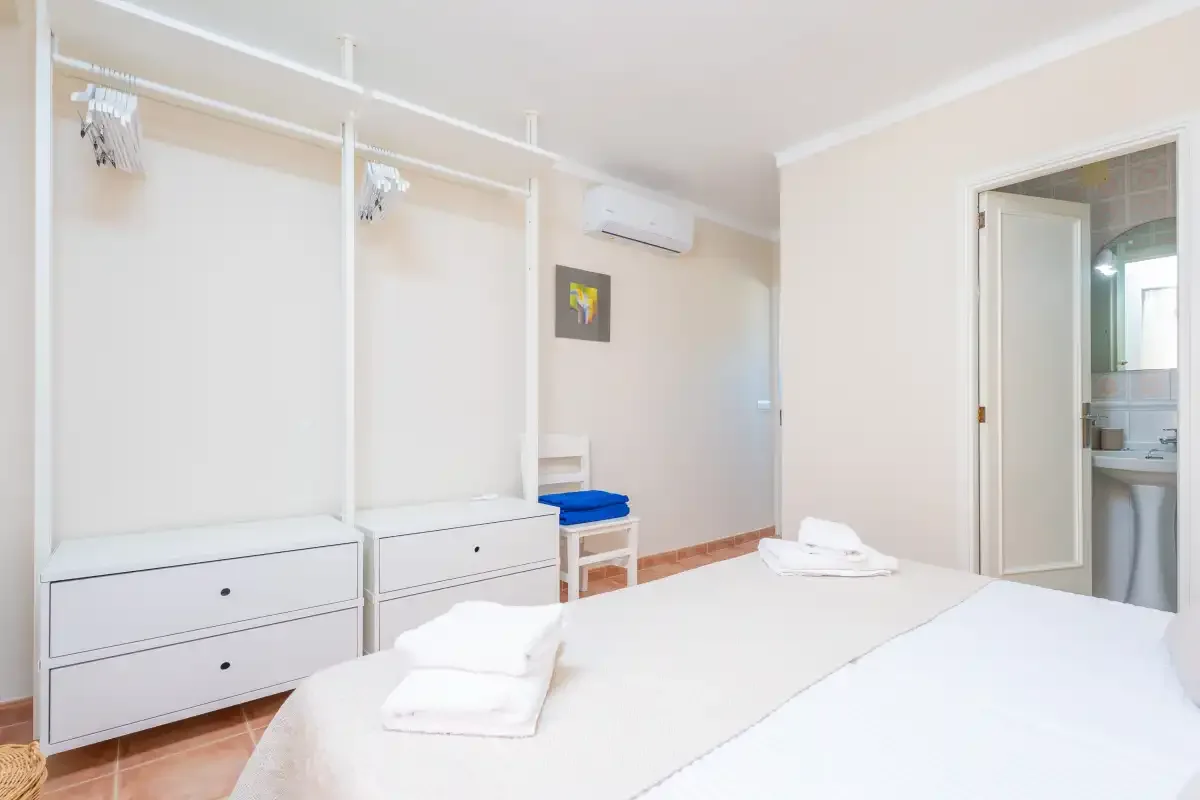 Un dormitorio luminoso con dos camas, armarios abiertos y una puerta al baño.