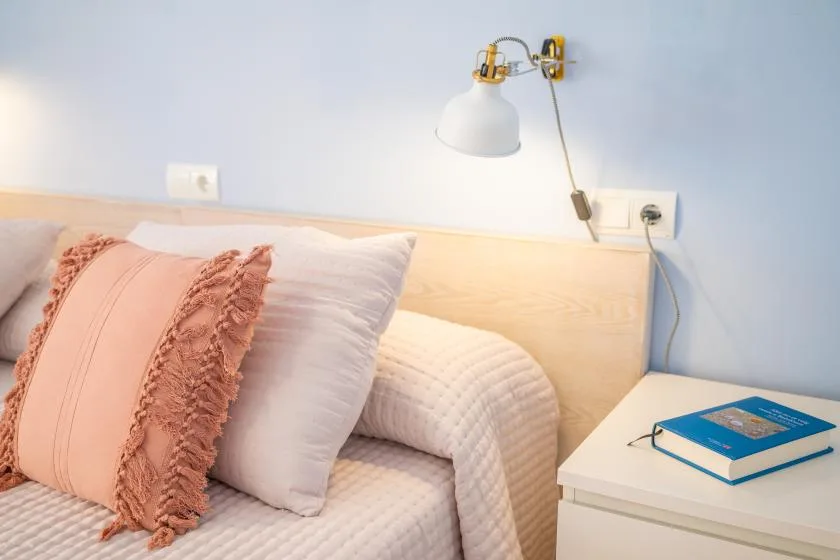 Un dormitorio con una cama, varias almohadas, una lámpara de pared y una mesita de noche.