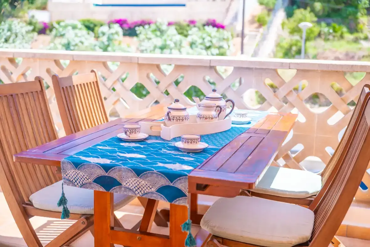 Una mesa de comedor en el patio está dispuesta con un mantel azul y un juego de té de cerámica.