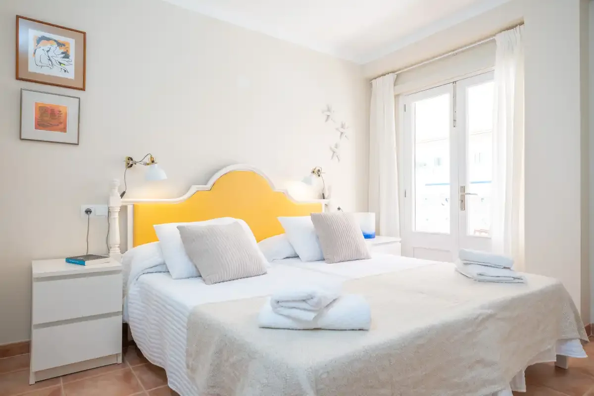 Un dormitorio luminoso con una cama doble bajo un cabecero amarillo.