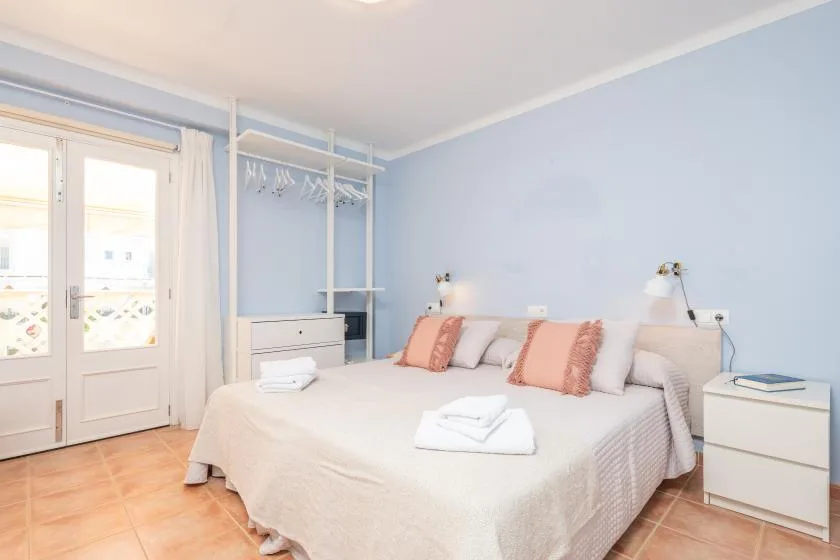 Un dormitorio con una cama doble, paredes azul claro y puertas al balcón.