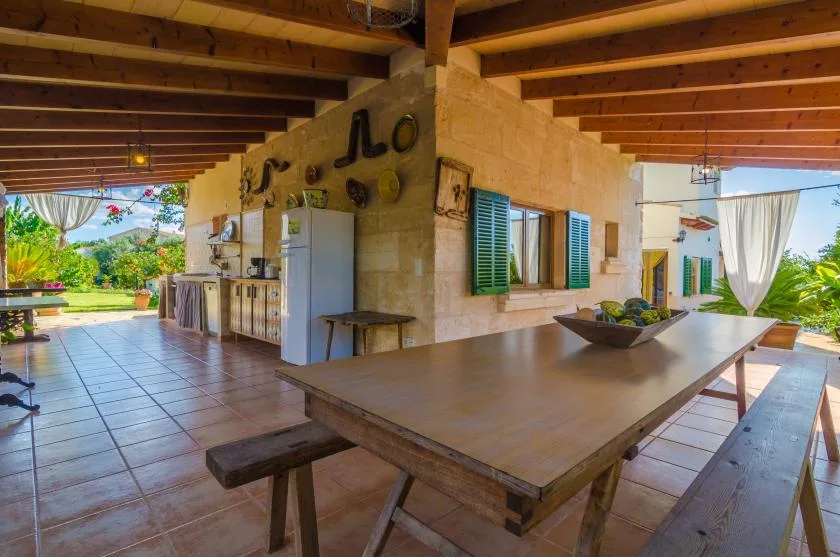 Un comedor exterior cubierto con una mesa larga de madera y vistas al jardín.