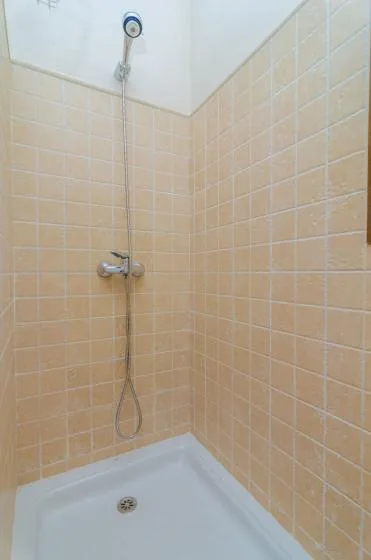 Una ducha revestida de azulejos con una alcachofa de mano sobre una base blanca.