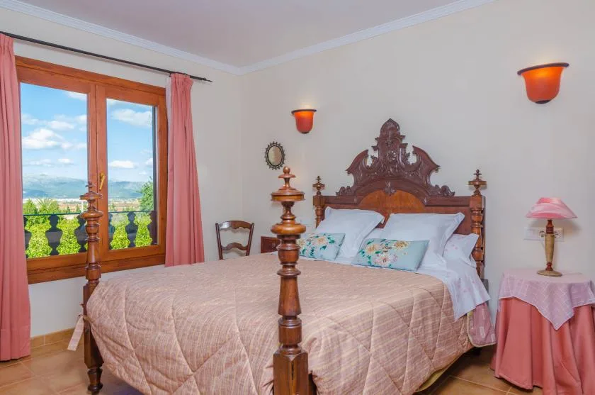 Un dormitorio con una cama grande, un cabecero de madera ornamentado y ventanas con vistas a zonas verdes.