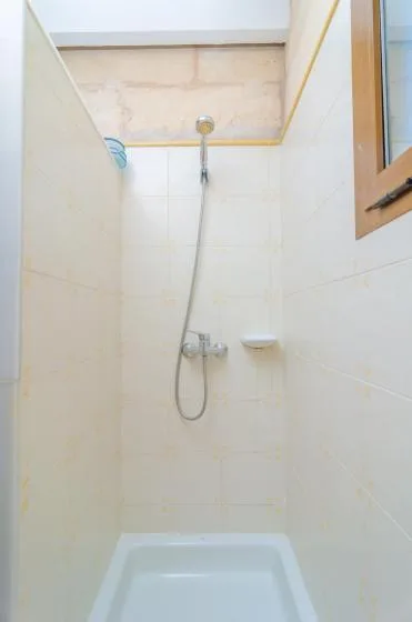 Una ducha de baño con azulejos, cabezal de mano y una pequeña repisa en la pared.