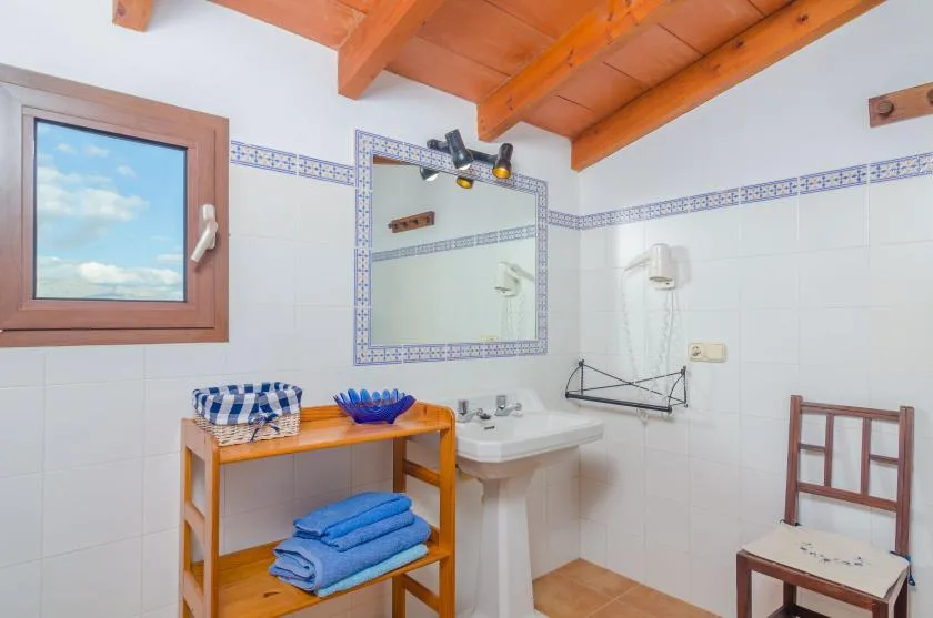 Un baño alicatado con lavabo, espejo de pared y toallas dobladas sobre una estantería de madera.
