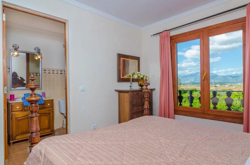 Dormitorio con una ventana grande que da a campos verdes y colinas lejanas.